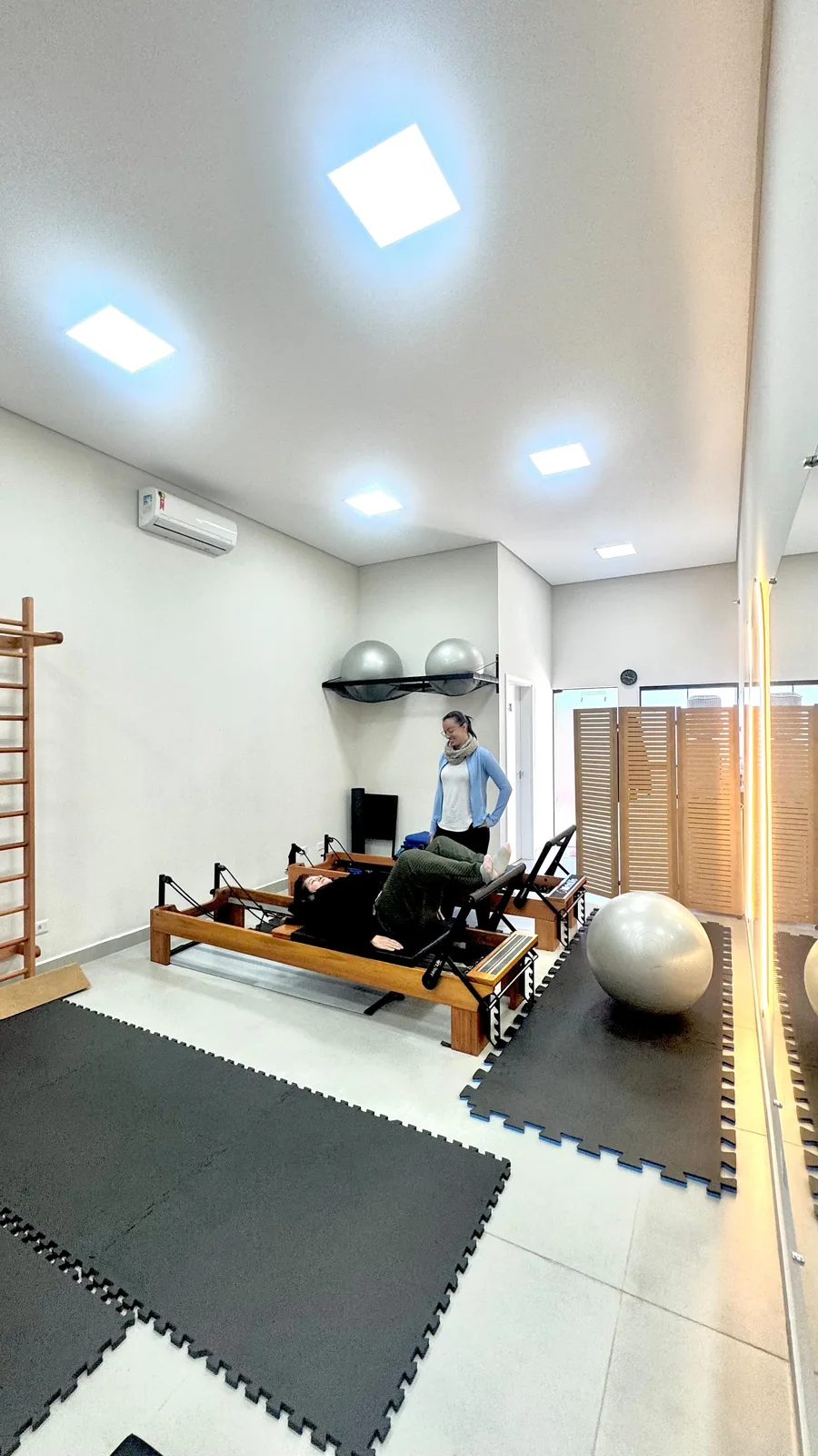 Sala de pilates ampla e iluminada, com Reformers de madeira e bolas na prateleira